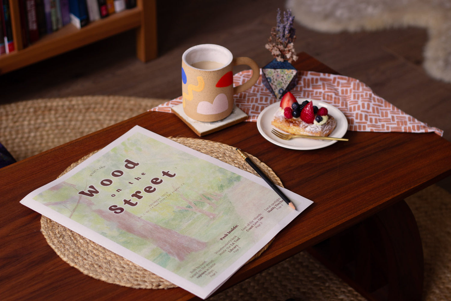 Wood on the Street newspaper laying on a wooden table, mug and pastry on the side